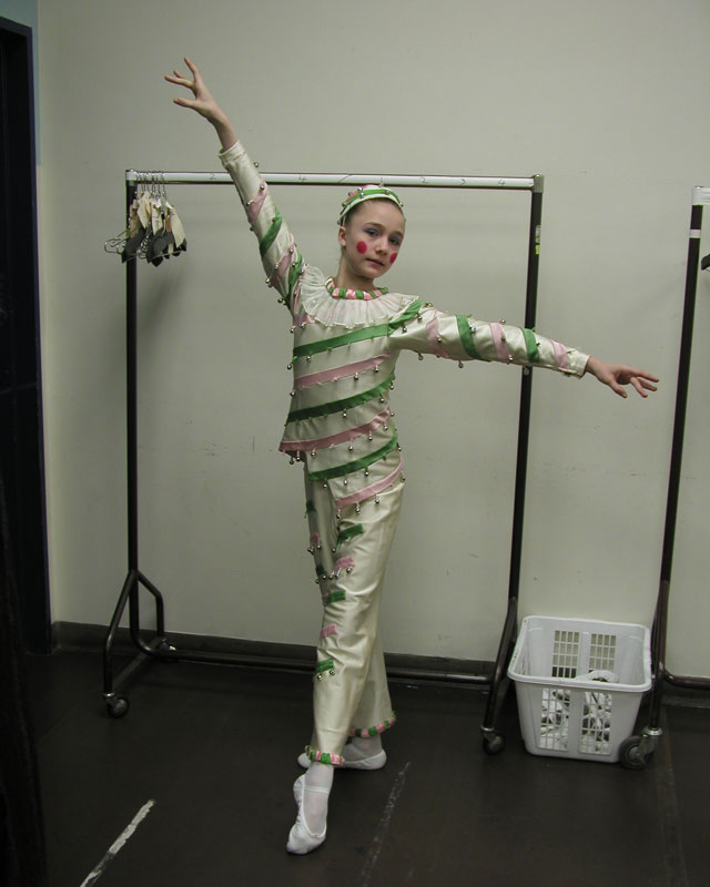 Cecilia Iliesiu as a young dancer in a white top and pants with green and white stripes.