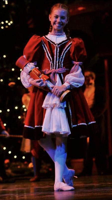 Juliet Prine stands on stage as a young dancer in a red costume.