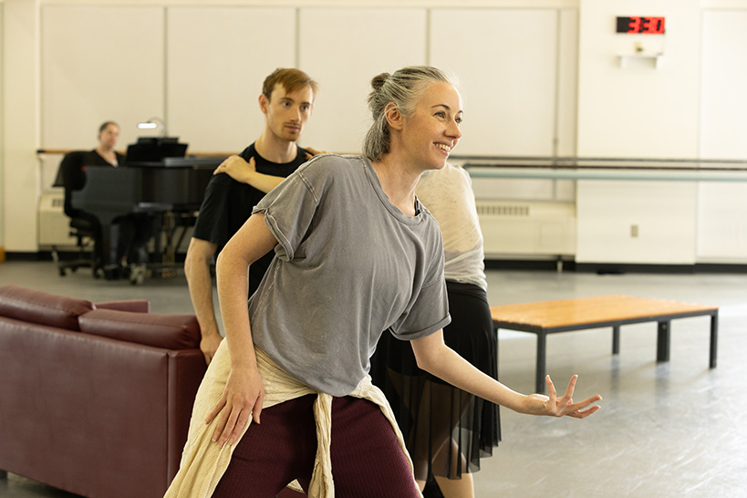 Dani Rowe smiles and demonstrates a step to two dancers in rehearsal.