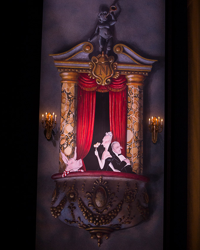A cartoon pig sits next to very fancy folks in an ornate theater box.