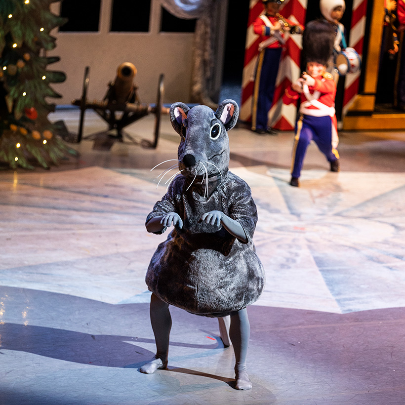 A dancer in a cartoonish mouse costume poses on stage.