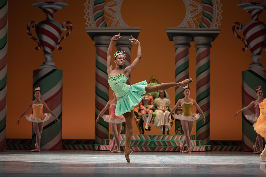 A dancer in a green tutu and tiara stands in arabesque.