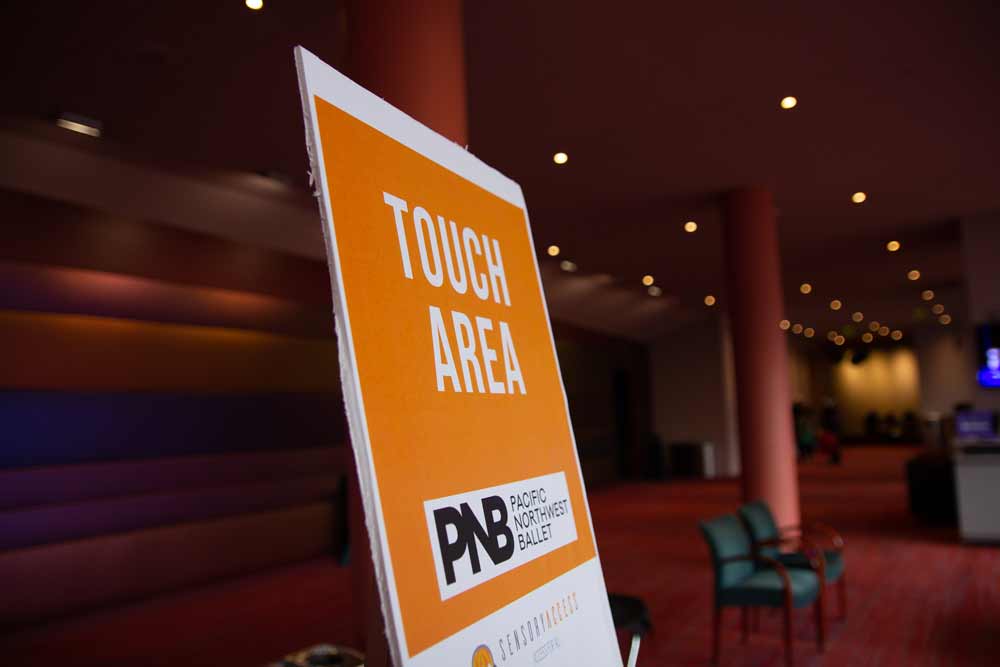 An orange sign with the words "Touch Area" stands in a theater lobby.