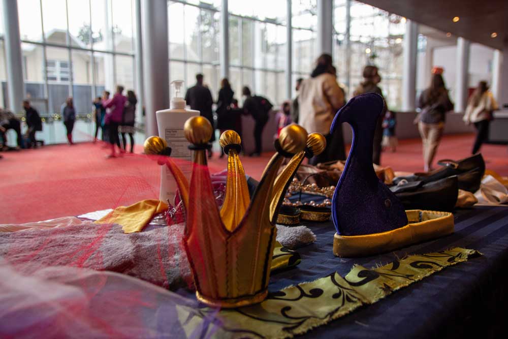 People walk past a table with cloth costume elements like a red crown and a blue hat in the shape of a peacock.