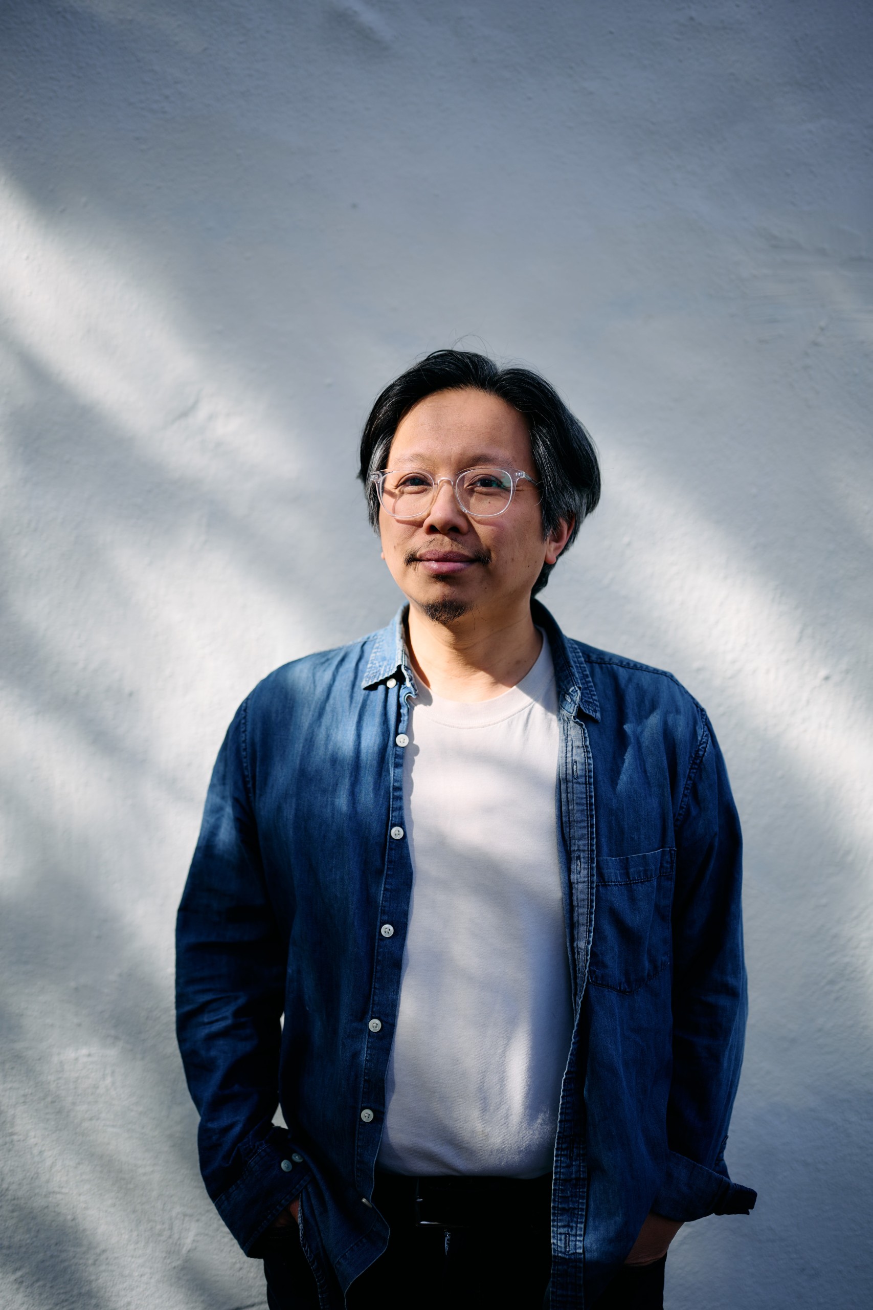 Tomo Nakayama Tomo Nakayama, wearing a denim shirt over a white t-shirt and wearing glasses.